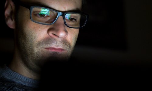 A man in glasses views a computer screen