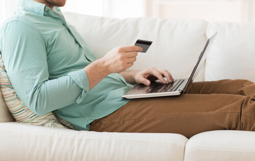 A person holding a bank card while using a laptop on a sofa